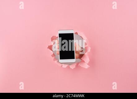 Femme tenant le smartphone dans un trou enveloppé sur fond rose, espace de copie Banque D'Images