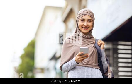 Joyeuse femme arabe marchant dans la rue, en utilisant le téléphone Banque D'Images