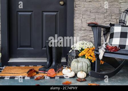 Véranda traditionnelle décorée pour l'automne avec bottes de pluie, gourdes de bruyère, citrouilles blanches, mamans et chaise à bascule avec coussin à carreaux de buffle Banque D'Images