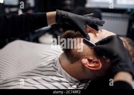 Barbier se raser un homme dans un salon de coiffure, gros plan Banque D'Images