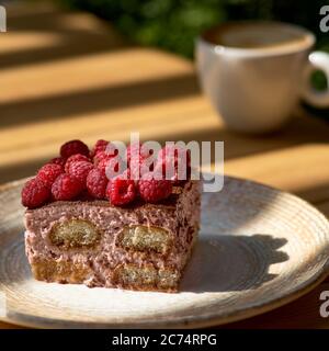 Tiramisu à la framboise sur une assiette noire sur une table en bois, matin, à l'aube. Banque D'Images