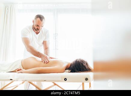 Homme de masseur barbu effectuant des manipulations de massage sur la zone lombaire pendant un massage corporel de jeunes femmes. Banque D'Images