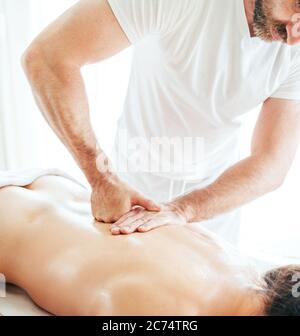 Homme de masseur barbu effectuant des manipulations de massage sur la zone de Scapula pendant le massage de corps de jeune femme. Banque D'Images
