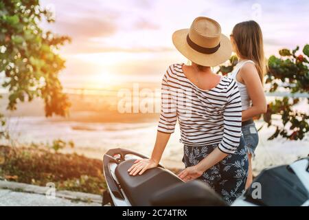 Deux filles voyageurs regardant sur le coucher de soleil sur la mer pendant leur motojorney Banque D'Images