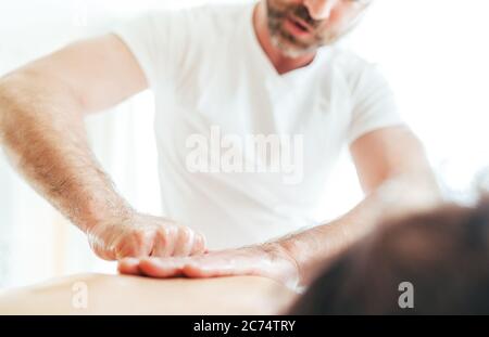 Homme de masseur barbu effectuant des manipulations de massage sur la zone de Scapula pendant le massage de corps de jeune femme. Banque D'Images