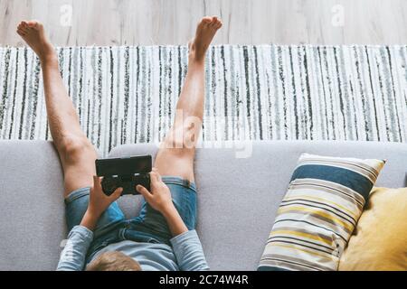 Garçon assis sur un canapé joue avec un smartphone et une manette de jeu vue du dessus de l'appareil photo. Concept des dispositifs électroniques et enfants Banque D'Images