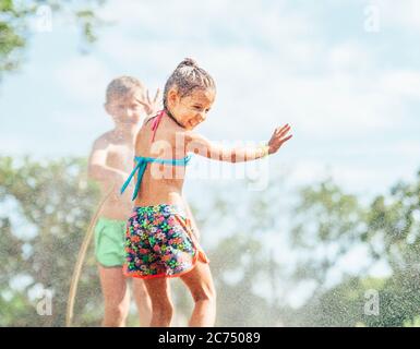 Deux enfants jouent avec l'eau saupoudrée dans le jardin d'été Banque D'Images