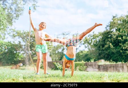 Les enfants heureux se métrompent dans le jardin d'été, éclaboussant l'eau et sautant Banque D'Images