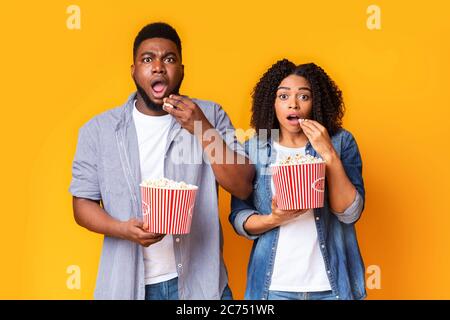 Film d'horreur. Un couple afro-américain choqué avec des seaux à maïs soufflé sur fond jaune Banque D'Images