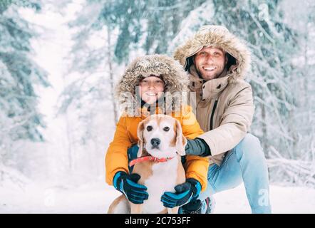 Père et fils vêtus de chaud capuche décontracté Parka Veste Outerwear marchant avec leur chien de beagle dans la forêt enneigée gai souriant visages portrait. PE Banque D'Images