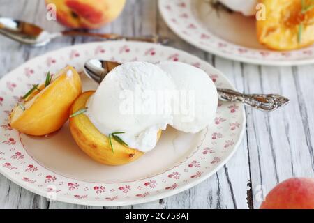 Vue en hauteur sur les pêches fraîches rôties maison cuites au sucre brun et aux branches de romarin frais et servies avec de la glace à la vanille. Mise au point sélective avec Banque D'Images