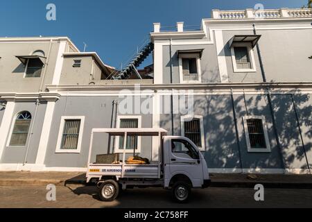 Pondichéry. Inde - février 2020 : un vieux bâtiment de l'ère française avec des fenêtres rectangulaires et des murs gris avec un tempo à quatre roues passé. Banque D'Images