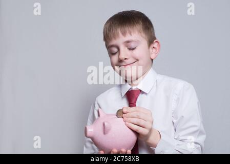 Happy boy met une pièce dans une banque de porc rose. Concept d'entreprise. Arrière-plan clair Banque D'Images