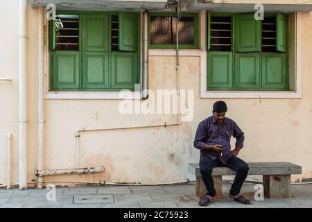 Pondichéry. Inde - février 2020 : un homme assis à l'extérieur d'une maison avec des fenêtres en bois vert pittoresque dans le style français dans la vieille ville. Banque D'Images