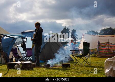 Préparation à la cuisson sur un feu de camp dans un campement de festival avec des nuages de pluie de tempête sombre et le soleil, Norfolk Banque D'Images