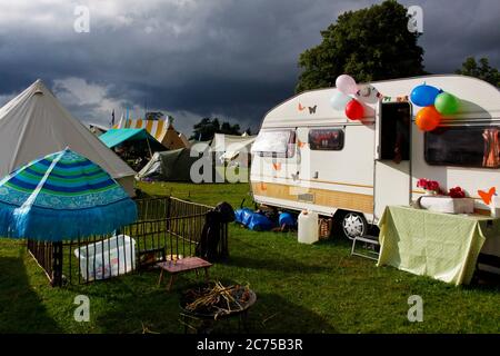 Terrain de camping avec tentes et caravane rétro dans un campement de festival avec des nuages de pluie et le soleil spectaculaires, Norfolk Banque D'Images