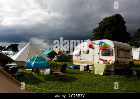 Terrain de camping avec tentes et caravane rétro dans un campement de festival avec des nuages de pluie et le soleil spectaculaires, Norfolk Banque D'Images