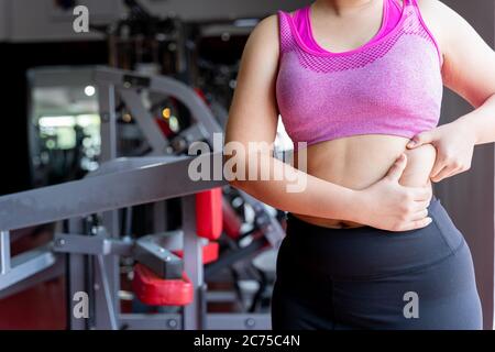 Femme de gras tenant le ventre gras excessif, le ventre gras en surpoids à la salle de fitness. Régime style de vie, perte de poids, muscle d'estomac, concept sain. Banque D'Images