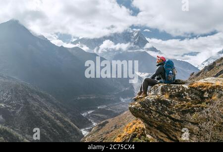 Jeune randonneur femelle assis sur le bord de la falaise et profitant de la vue sur les sommets de la montagne pendant l'itinéraire de randonnée Everest base Camp (EBC) près de Phortse, N Banque D'Images