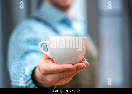 Gros plan de Man Barista étirant la main avec une tasse à café. Petit déjeuner parfait. Concept de séjour à la maison. Préparation du café par amateur à la cuisine maison Banque D'Images