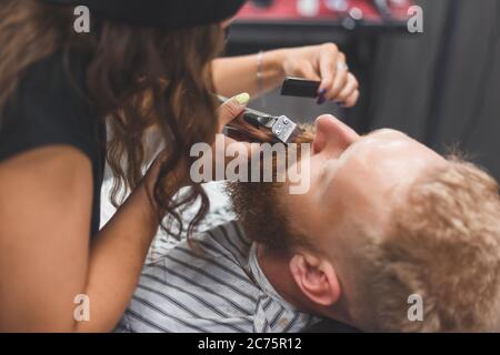 Un homme dans un salon de coiffure. Femme barbier tachant la moustache. Femme de coiffure dans le masque. Banque D'Images