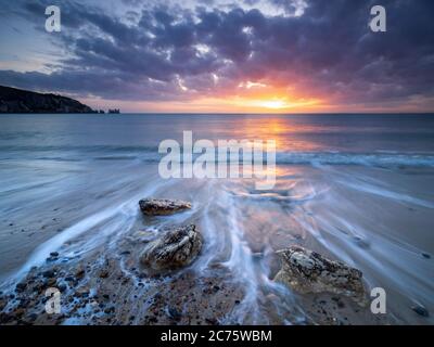 Un coucher du soleil brille sur les roches d'Alun Bay sur l'île de Wight, en mettant en évidence les sentiers laissés par les vagues à marée haute. Banque D'Images