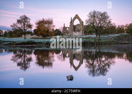 Les ruines de l'abbaye de Bolton dans Wharfedale, Yorkshire, se reflètent dans la rivière Wharfe sur un beau calme, frosty matin d'automne. Banque D'Images