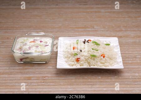 Légumes Pulav ou Pulao, faits à base de riz basmathi, légumes et épices indiennes.Raita comme plat d'accompagnement disposé dans un plat blanc carré de table avec couleur bois Banque D'Images