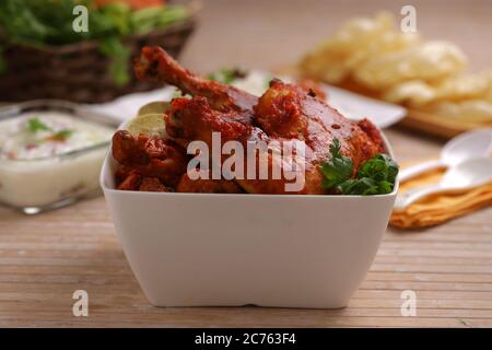 Poulet Tandoori épicé garni de feuilles de citron et de coriandre dans un bol carré blanc avec fond en bois, foyer sélectif Banque D'Images