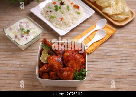 Poulet Tandoori épicé garni de feuilles de citron et de coriandre dans un bol carré blanc avec fond en bois, foyer sélectif Banque D'Images