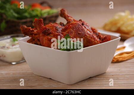 Poulet Tandoori épicé garni de feuilles de citron et de coriandre dans un bol carré blanc avec fond en bois, foyer sélectif Banque D'Images