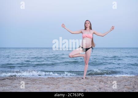 Femme enceinte médite sur la plage. Pratique de yoga. Lumière douce du soir Banque D'Images