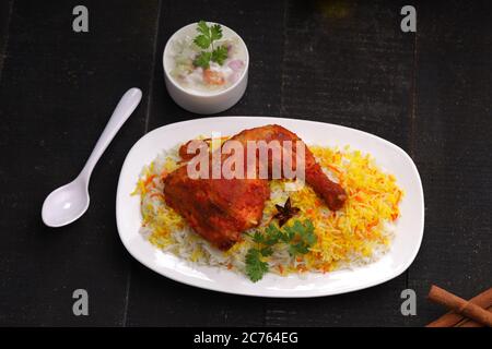 Poulet biryani , cuisse de poulet Tandoori avec riz basmathi et raita ou raitha comme plat d'accompagnement disposé dans une assiette blanche avec fond noir ou textur Banque D'Images