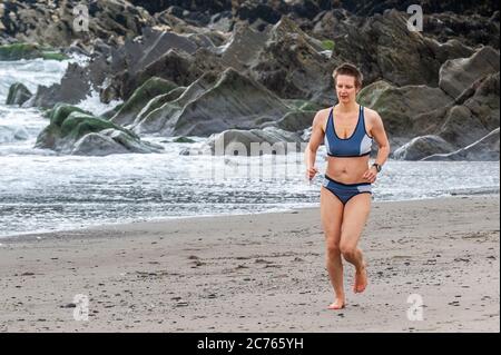 Owenahincha, West Cork, Irlande. 14 juillet 2020. Une femme court sur la plage de Red Strand, à l'ouest de Cork, malgré le temps froid. Crédit : AG News/Alay Live News Banque D'Images