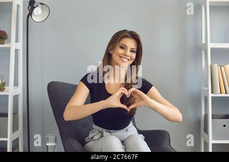 Concept de rencontres en ligne. Jeune femme romantique montrant le cœur avec les mains pendant la conférence web avec son petit ami à l'intérieur Banque D'Images