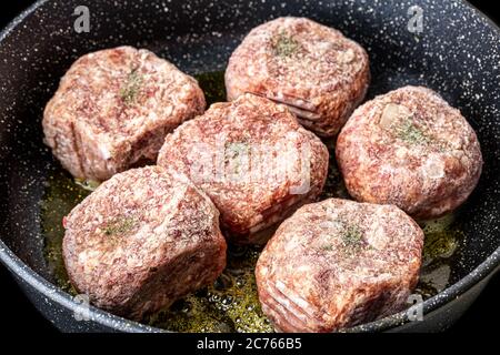 Côtelettes de bœuf cru, chauffées dans une poêle noire en céramique avec de l'huile végétale. Le processus de friture des steaks. Cuisine traditionnelle. Banque D'Images
