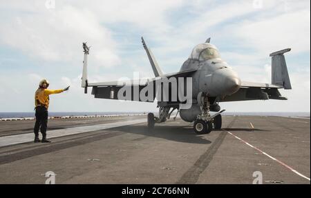 Une veste jaune de la Marine américaine dirige un avion de chasse F/A-18e Super Hornet, des Diamondbacks du Strike Fighter Squadron 102, pour se positionner sur le pont de vol du porte-avions de la classe Nimitz USS Ronald Reagan pendant les opérations du 21 juin 2020 en mer des Philippines. Banque D'Images