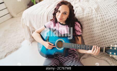 Jeune femme jouant de la guitare dans la chambre. Jeune femme jouant de la guitare dans son lit. Elle aime son temps libre. Belle fille jouer de la guitare dans un confortable Banque D'Images