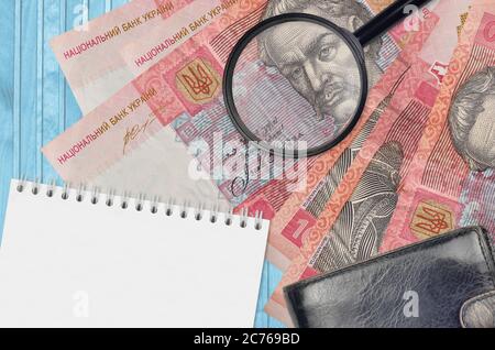 10 billets de hryvnias ukrainiens et loupe avec sac à main noir et bloc-notes. Concept de fausse monnaie. Recherchez les différences dans les détails sur mone Banque D'Images