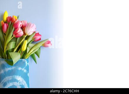 Bouquet de tulipes colorées dans un sac textile sur un arrière-plan bleu avec espace de copie Banque D'Images