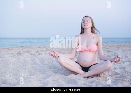 Femme enceinte assise sur une plage et médite. Douce lumière du soir, plage déserte. Banque D'Images