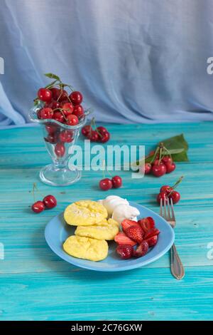 Portion de cheesecakes jaunes maison avec crème sure et baies fraîches sur une table en bois bleu. Petit déjeuner délicieux et sain Banque D'Images