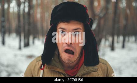 L'homme grimace dans la forêt en hiver. Portrait d'un homme fou portant un chapeau à rabat et un visage grimaquant en forêt d'hiver. Banque D'Images