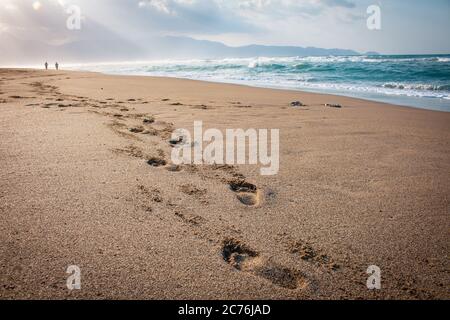 Belle plage avec des empreintes dans le sable. Les amateurs de marche sur la plage au coucher du soleil et empreintes de pieds laissant sur la plage. Silhouettes de coup Banque D'Images