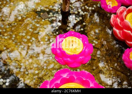 Bougies flottantes en forme de fleur de lotus rose sur les eaux de la fontaine avec des pièces de monnaie visibles au fond des fontaines jetées pour la chance. Banque D'Images