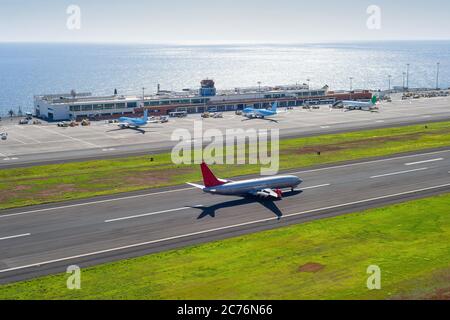 Vue aérienne de l'aéroport international de Funchal avec avions par terminal, avion en train de descendre à l'aérodrome, paysage marin en arrière-plan avec des rayons du soleil Banque D'Images