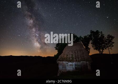 Ancienne ferme de grange abandonnée avec quelques arbres derrière elle a tourné dans la nuit contre un ciel étoilé avec la voie laiteuse galactique noyau vu ci-dessus tourné à Dumesti Banque D'Images