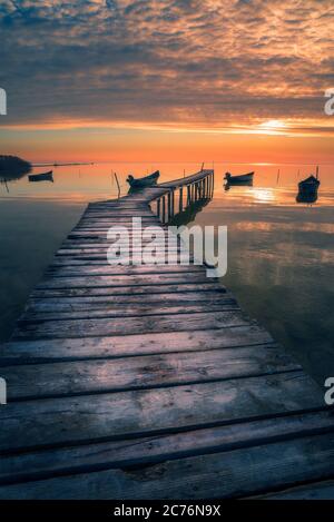 Ponton en bois sur un lac au lever ou au coucher du soleil avec plusieurs bateaux de pêche Banque D'Images