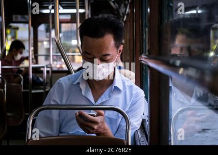 Un passager portant un masque de protection utilise son téléphone dans un tramway à Hong Kong. Le gouvernement de Hong Kong impose de nouvelles mesures strictes de distanciation sociale et le port obligatoire de masques pour les personnes utilisant les transports publics. Banque D'Images