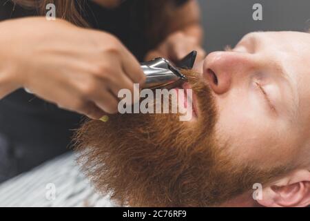 Un homme dans un salon de coiffure. Femme barbier tachant la moustache. Femme de coiffure dans le masque. Banque D'Images